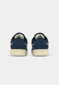 Navy blue canvas sneakers with a textured finish, white stitching, and contrasting cream rubber soles. Rounded back design, minimal perforations.