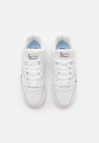 White sneakers with a perforated texture, featuring blue accents, flat laces, and a logo on the tongue. Rounded shape and cushioned sole.