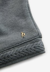 Szary dzianinowy beanie o plecionej strukturze u podstawy, z małym złotym logo wyszytym z boku. Miękka tkanina i dopasowany krój.