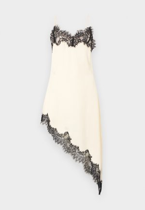Crèmekleurige satijnen slipdress met zwarte kanten afwerking bij de buste en een asymmetrische zoom, voorzien van dunne spaghetti bandjes tegen een effen achtergrond.