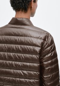 Doudoune marron avec un design matelassé horizontal, tissu lisse et brillant, et un col court. Vue de dos montrant une silhouette épurée.