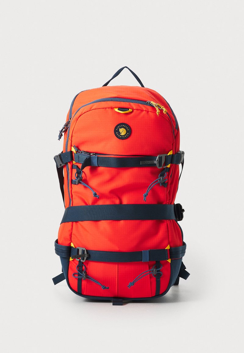 Mochila de nylon roja con múltiples compartimentos, correas ajustables en navy, acentos reflectantes y un logo circular en la parte frontal.