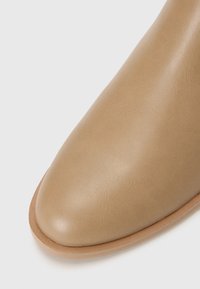 Bottine en cuir tan avec un bout pointu et une texture lisse. Présente un design minimaliste avec une semelle de couleur claire.
