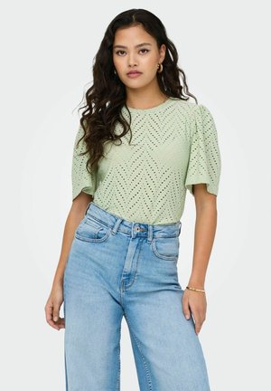 Haut vert clair à manches courtes avec un design texturé présentant des motifs découpés et un col rond, associé à un jean en denim bleu taille haute.