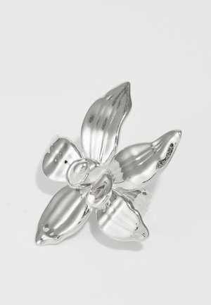 Ezüst orchidea bross négy textúrázott szirommal, középen kerek részlettel, sima felülettel, fényes bevonattal és finom barázdákkal a sziromon.