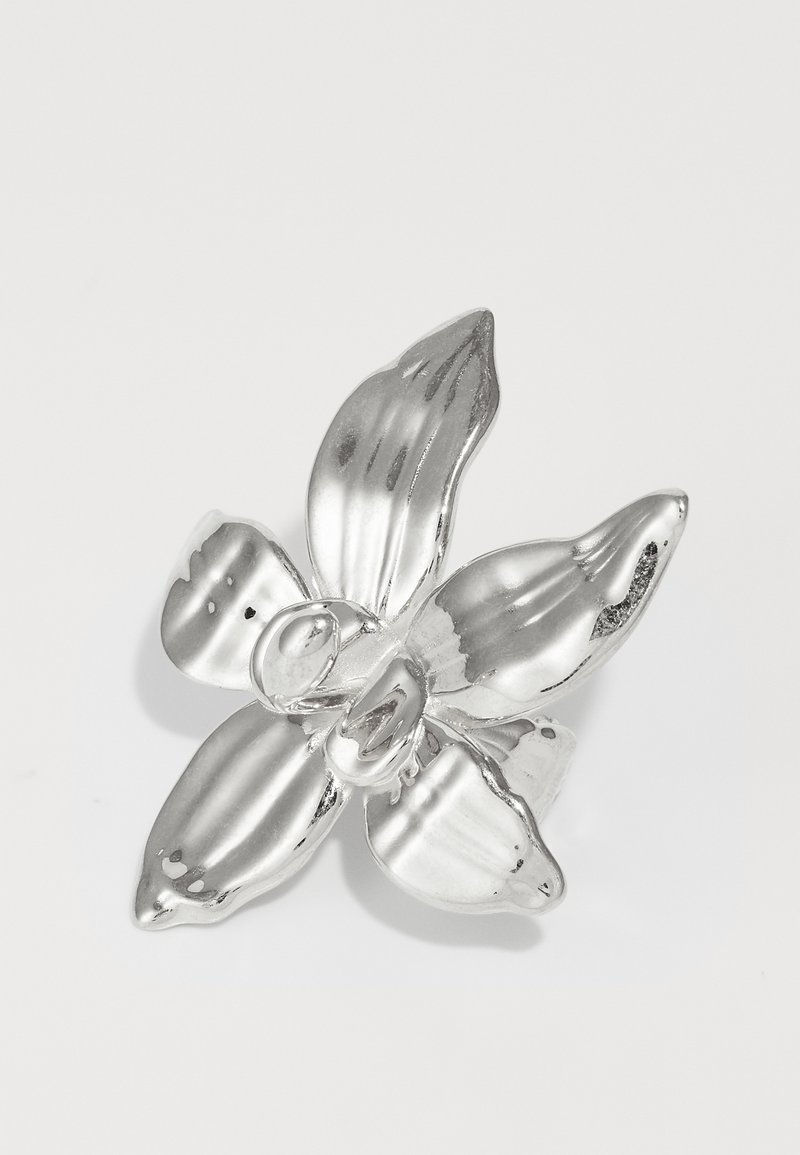 Stříbrná brož s orchidejí se čtyřmi texturovanými okvětními lístky, centrálním kulatým detailem, hladkým povrchem, lesklým finišem a jemnými rýhami na okvětních lístcích.