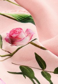 Tela elástica con fondo rosa y un estampado floral de rosas pink y hojas verdes, que muestra una textura suave y colores vibrantes.