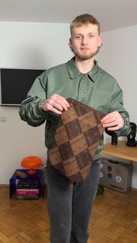 Brown checkered fabric piece with a textured surface, featuring contrasting dark and light squares, held by a person in a green jacket.
