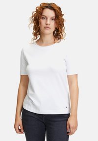 Biała bawełniana koszulka z krótkim rękawem, okrągłym dekoltem, luźnym krojem, z małym logo akcentującym przy dolnym brzegu i gładką fakturą.