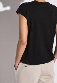 Svart kortärmad t-shirt i mjuk tyg, med avslappnad passform och en enkel rund halsringning. Kombination med ljusbeiga byxor.