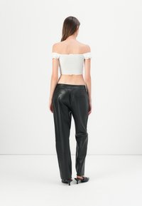 Hvit avdelte croppet topp med volangkanter, parret med tettsittende svarte skinnbukser. Glatte teksturer og skreddersydde designdetaljer synlige.