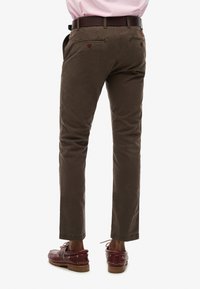 Ciemnobrązowe chinosy o prostym kroju, z dwoma tylnymi kieszeniami z czerwonymi guzikami i paskiem przewleczonym brązowym skórzanym paskiem.