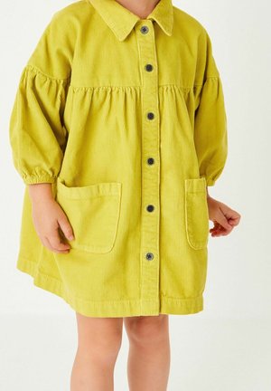 Vestido de pana amarillo con cuello, cierre de botones en la parte delantera y mangas abullonadas. Cuenta con dos bolsillos frontales y un corte relajado.