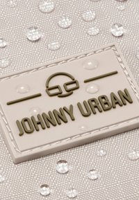 Tessuto grigio con un motivo testurizzato e gocce d'acqua. Un'etichetta bianca riporta "JOHNNY URBAN" in caratteri verdi e un logo.