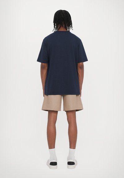 T-shirt en coton bleu marine avec une coupe décontractée, des manches courtes et un col rond, associé à un short beige et des chaussettes blanches.