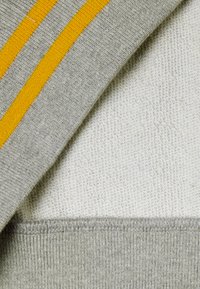 Tessuto grigio a maglia con strisce gialle, piegato sopra un tessuto bianco in spugna testurizzato e bordo a costine grigio.