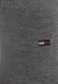 Grå bomullssokk med ribbet tekstur og en logo med røde, hvite og blå striper nær kanten. Mykt, middels tykt stoff.
