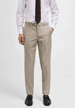 Beige skræddersyede bukser med en glat tekstur, lige snit og frontfolder, parret med en hvid skjorte og et mørkt slips. Sorte loafers vist.