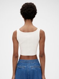 Ribbed bílé crop top s kulatým výstřihem, v kombinaci s vysokým pasem modrých džínsů. Hladká textura s minimálními švy a bez viditelných zapínání.