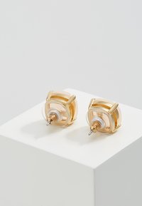 Gold-tone geometric stud earrings with translucent accents, a central white disc, and a metal pin for fastening.