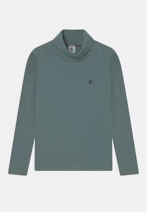 Zielona koszulka z długim rękawem i golfem, z małym ciemnym logo żaglówki na lewej piersi, ułożona na płasko na białym tle.