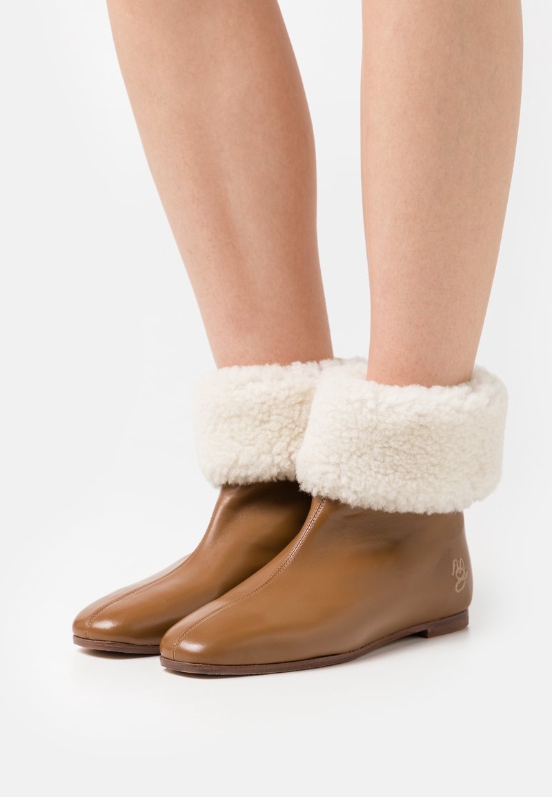 Stivaletti in pelle marrone con un morbido risvolto in shearling bianco, punta affusolata e suola piatta. Dettaglio del logo ben visibile sul lato.
