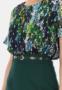Granatowa bluzka w kwiaty z zielonymi, niebieskimi i żółtymi akcentami, z krótkimi falbaniastymi rękawami i czarnym paskiem, w zestawie z zieloną spódnicą.