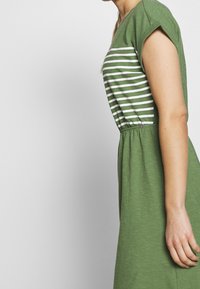 Grünes Kleid mit kurzen Ärmeln, ausgestattet mit vertikalen weißen Streifen im oberen Teil und einem elastischen Taillenbund. Der Stoff hat ein weiches, strukturiertes Aussehen.