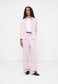 Ανοιχτό μωβ σακάκι με ταίριασμα πλατιά παντελόνια, με κουμπί στο μπροστινό μέρος, δύο πλάγιες τσέπες και λευκό τοπ από κάτω.