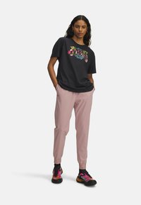 Black t-shirt with colorful floral design, pink athletic pants with tapered legs, and black multicolored sneakers with textured soles.