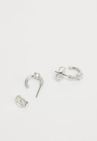 Silver hoop earrings featuring a curved design, adorned with clear rhinestones and a heart-shaped post. Reflective, smooth metal finish.