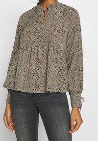 Blusa beige morbida con motivo a pois blu navy, scollatura arricciata, dettaglio con fiocco e pieghe arricciate. Maniche lunghe con polsini elasticizzati.