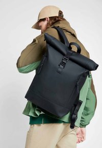 Black roll-top backpack made of waterproof material, featuring adjustable straps, a front buckle, and subtle branding.
