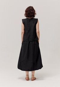 Czarna sukienka bez rękawów z dopasowaną górą i rozkloszowaną, sięgającą kostek spódnicą. Charakteryzuje się prostym wzornictwem z delikatnymi szwami. Uzupełniona beżowymi sandałami.