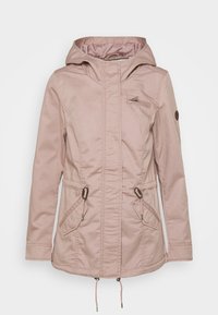 Chaqueta impermeable de color rosa claro con capucha, cintura ajustable con cordón, dos bolsillos delanteros y un bolsillo en el pecho con cremallera. Presenta una textura suave.