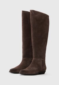 Bottes en suède marron hauteur genou avec une texture lisse, des orteils ronds et une discrète fermeture éclair latérale. Elles présentent un talon plat et des accents matériels minimalistes.