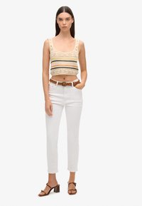 Gehaakte crop top met gestreept ontwerp in beige en multikleur; gecombineerd met witte, nauwsluitende jeans en een gevlochten bruine riem. Bruine sandalen met hakken.