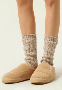 Beige kordfløjlssandaler med et quiltet design og gummisål, parret med stribede strikkede sokker i beige og krem.