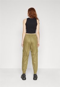 Svart ärmlös crop top som matchas med olivgröna cargobyxor med sidofickor, elastisk midja och avsmalnande muddar. Matt yta.