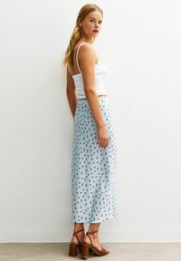 Light blue floral midi skirt with a flowing design, featuring small red flower patterns, paired with a white fitted tank top and brown heeled sandals.