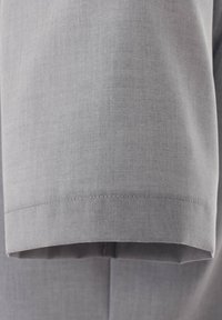 Jasnoszara rękaw z gładką fakturą, z przeszytym wykończeniem i łagodnym łukiem przy mankiecie, część dopasowanego ubrania.