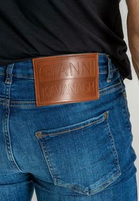 Traperice tamnog pranja imaju veliki, reljefni smeđi kožni paket s natpisom "GIANNI KAVANAGH" na stražnjem dijelu struka.