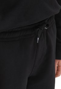 Pantalones de chándal negros de tela suave, con una cintura elástica y cordón, bolsillos laterales y detalles de costura sutiles.
