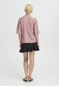 Helle rosa, strukturierte Bluse mit kurzen Puffärmeln, kombiniert mit einem schwarzen, schwingenden Rock. Verfügt über ein einfaches, gerades Rückendesign.