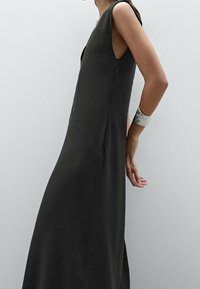 Tummanharmaa hihaton mekko, jossa on syvä V-pääntie, rento siluetti, sivuhalkiot ja sileä rakenne, yhdistettynä metalliseen rannerenkaaseen.