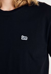 T-shirt in cotone nero con collo rotondo, dotato di un piccolo logo ricamato bianco "Lee" sulla parte sinistra del petto. Texture liscia.