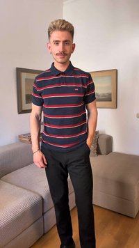 Μπλέ πόλο πουκάμισο με κόκκινες και λευκές οριζόντιες ρίγες, κοντά μανίκια και γιακά, συνδυασμένο με μαύρο παντελόνι και καθισμένο σε έναν υφασμάτινο καναπέ.