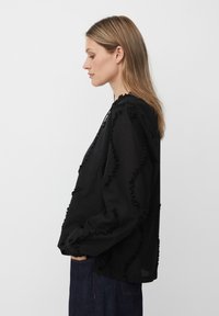 Blusa nera con rouches testurizzati lungo le cuciture, maniche lunghe e vestibilità rilassata. Tessuto leggero e colletto tondo semplice.