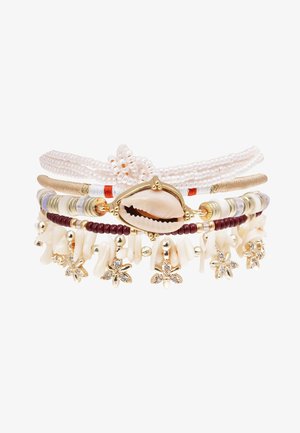 Bracelet multi-couches comprenant des coquillages blancs, des accents dorés et des perles bordeaux. Design texturé avec des charms floraux et des perles. Thème côtier élégant.