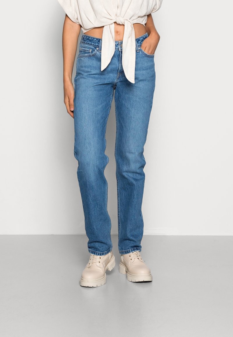Jean droit bleu clair en denim, avec un design classique à cinq poches, associé à des chaussures à plateforme beige.